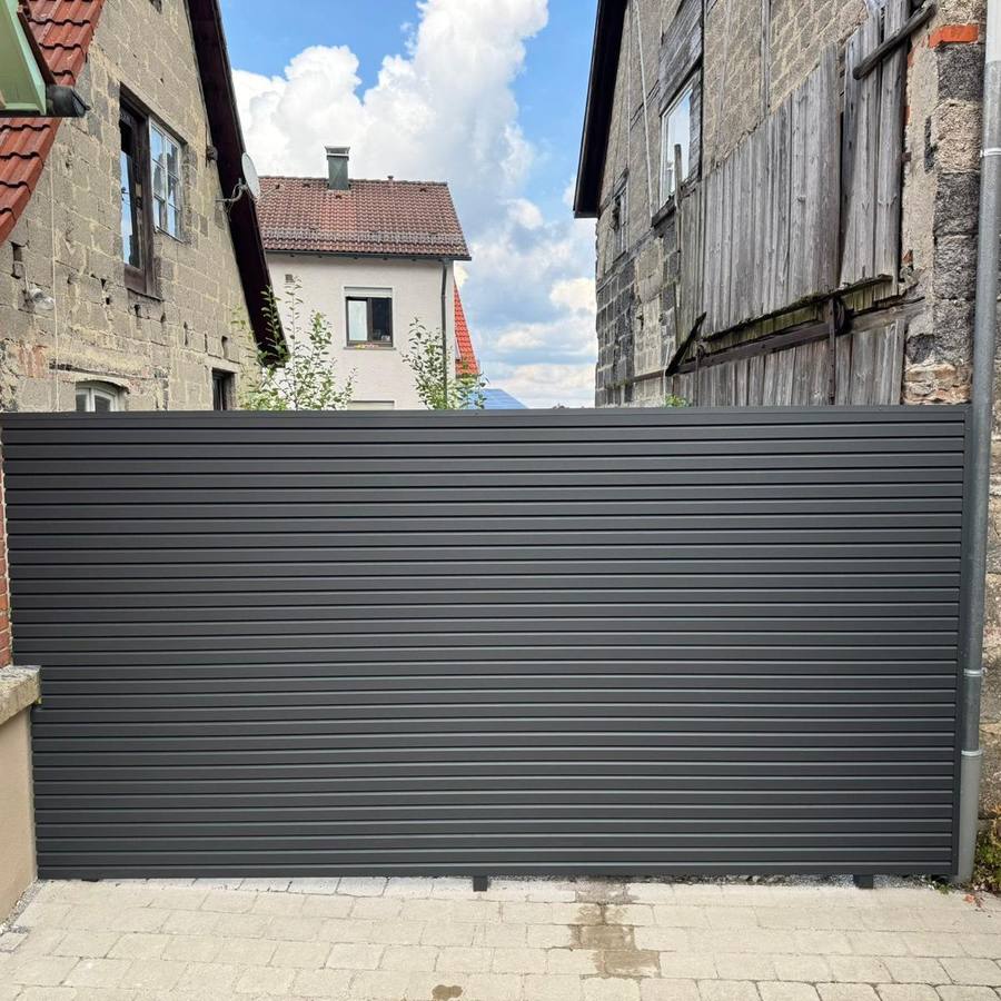 Anthrazitfarbenes Zauntor zwischen zwei Gebäuden